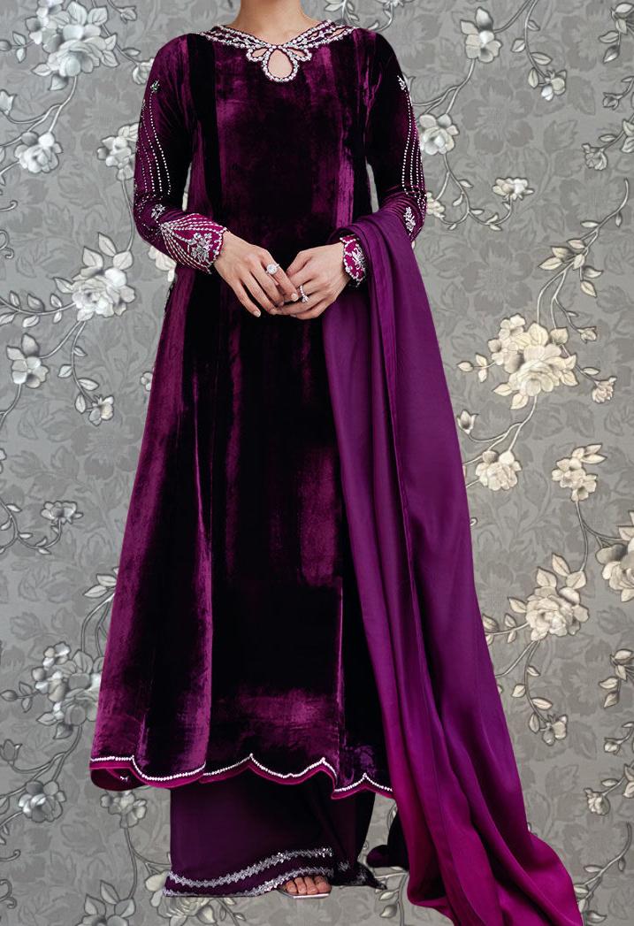 A person wearing a long, purple velvet dress with a matching purple shawl, standing against a gray floral background.
