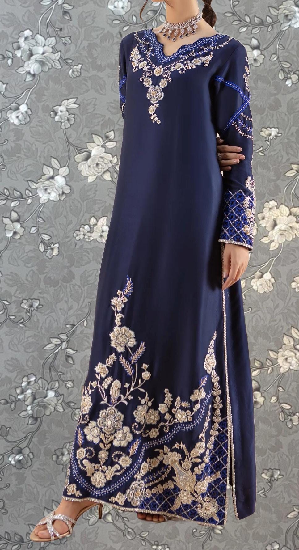 A woman wearing a long, navy blue dress with intricate gold embroidery and floral patterns.