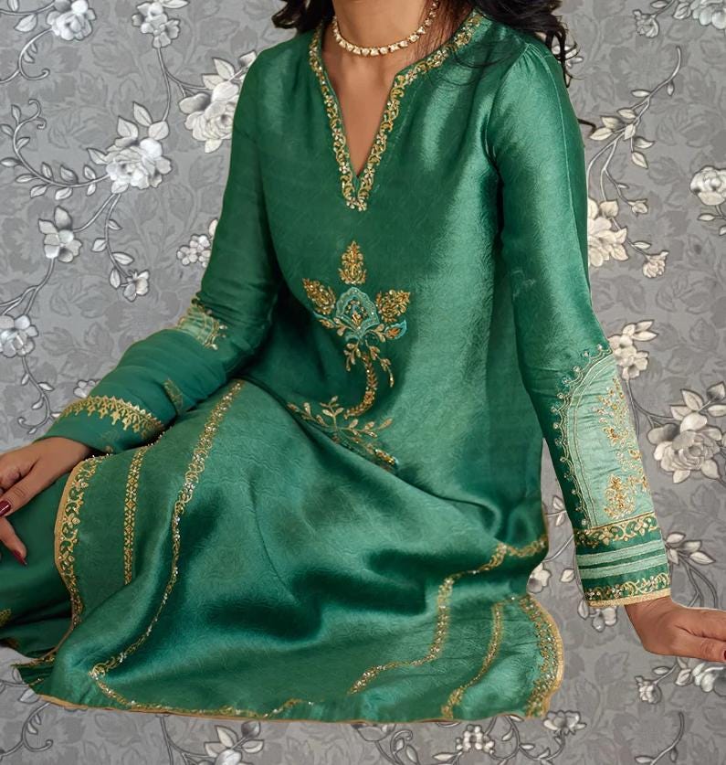 A woman wearing a green dress with gold embroidery and a floral pattern on the front.