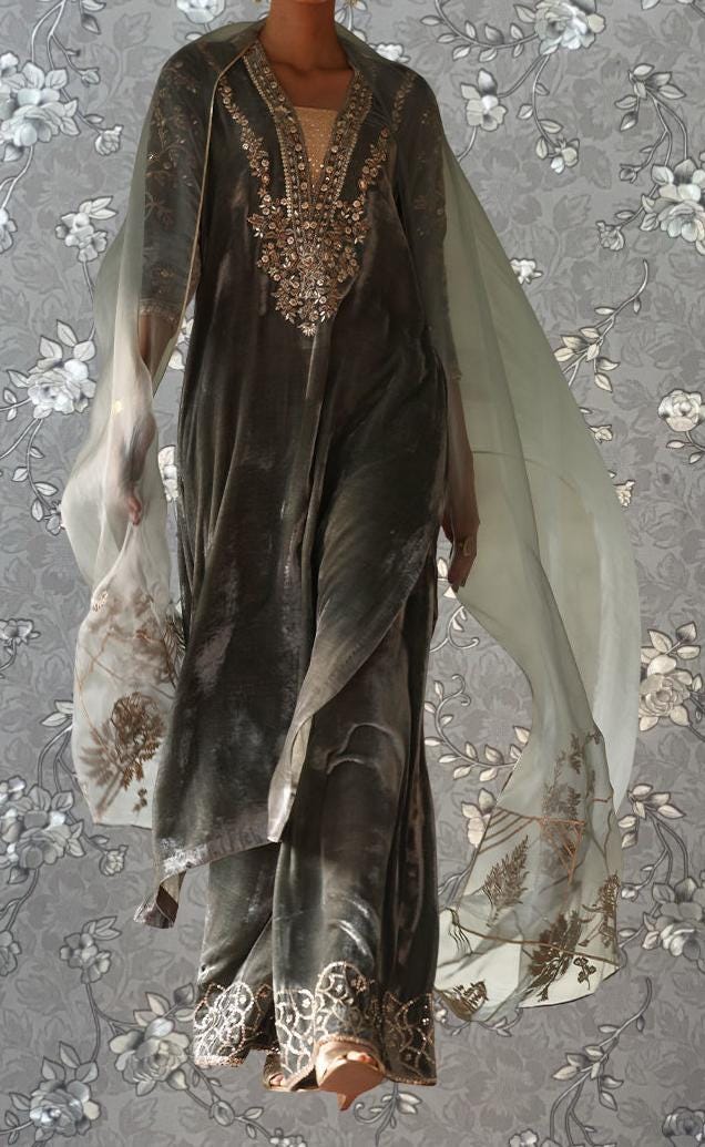 A woman wearing a long, gray dress with intricate embroidery and a flowing, sheer white shawl draped over her shoulders.