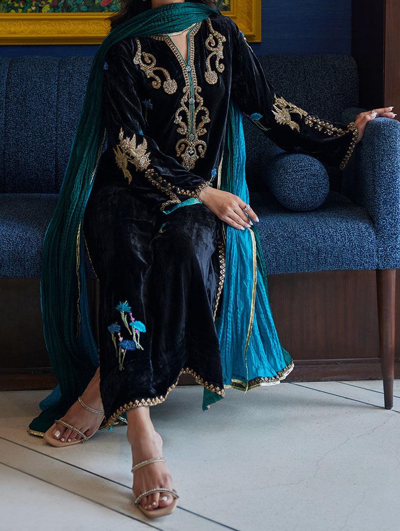 A woman wearing a black and blue dress with gold embroidery is sitting on a blue couch.