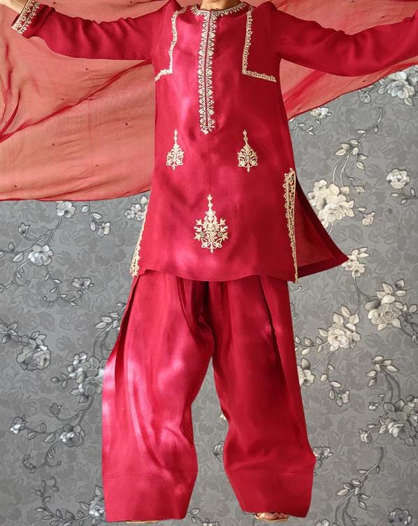 A red and gold outfit with intricate embroidery, including a red and gold jacket and matching red and gold pants, is displayed against a gray floral background.