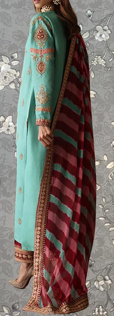 A woman wearing a turquoise and red patterned dress with a red and green striped shawl draped over her shoulders.