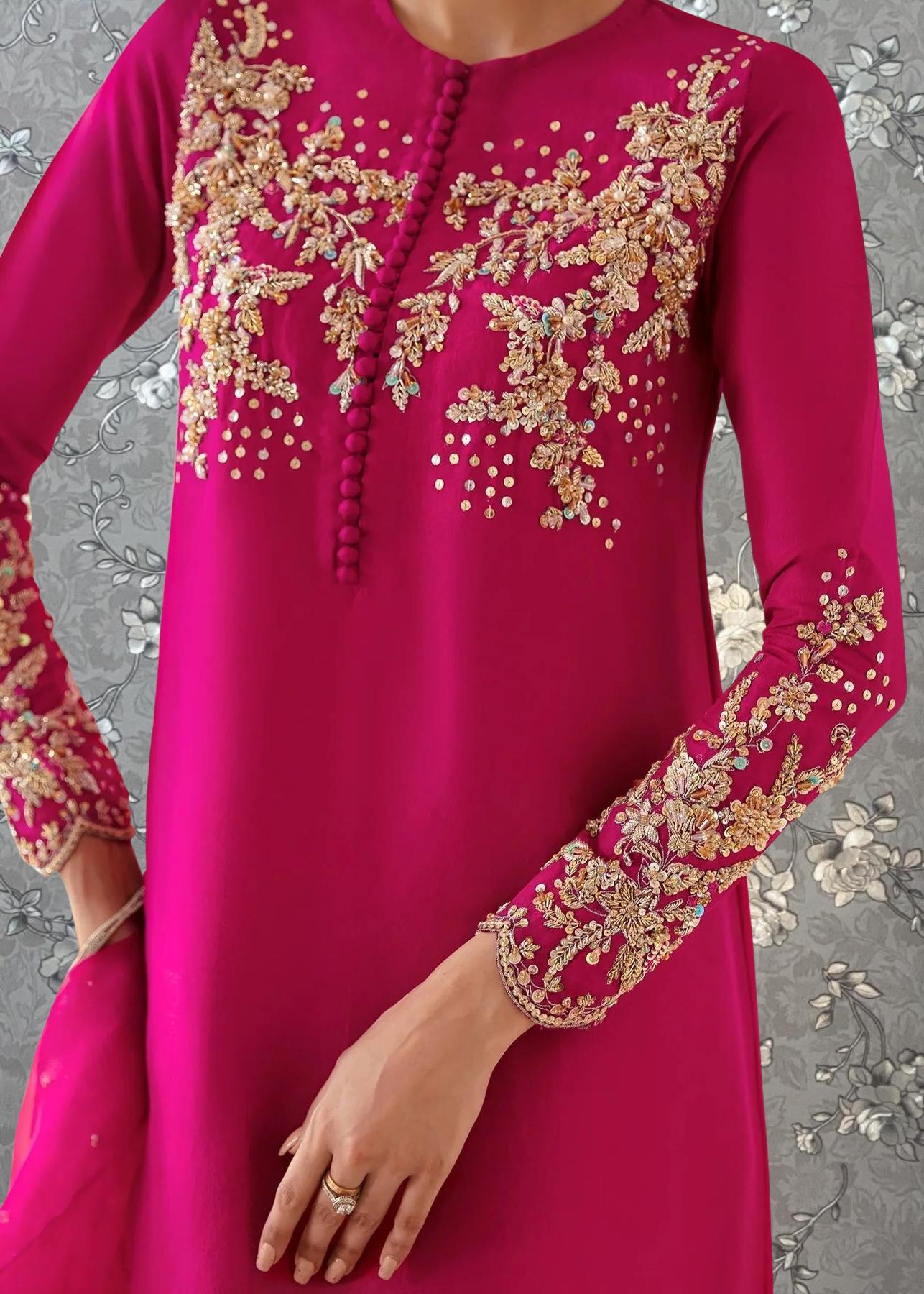 A close-up of a person wearing a long-sleeved pink dress with intricate gold embroidery on the sleeves and neckline.