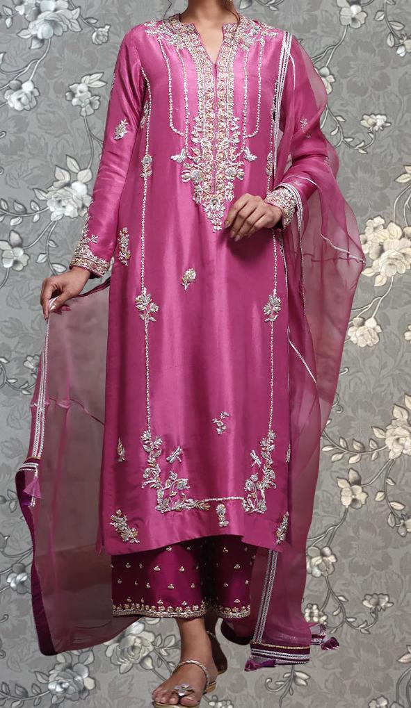 A woman wearing a long pink dress with intricate embroidery and a matching pink shawl.