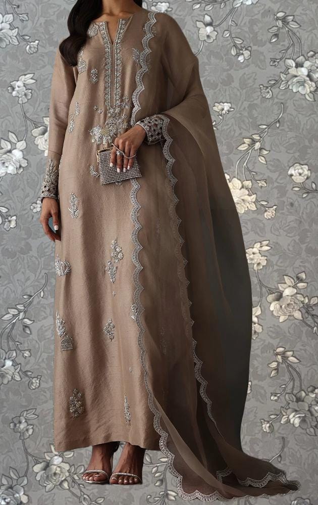 A woman wearing a long, beige dress with intricate embroidery and a matching shawl, standing against a floral patterned background.
