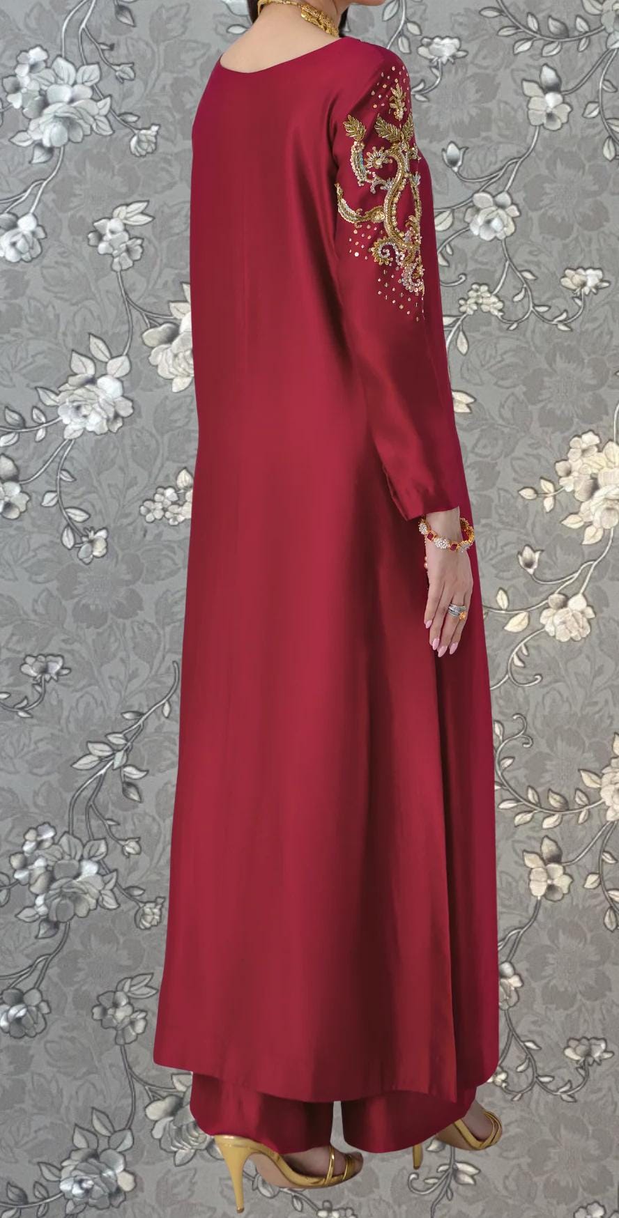 A person wearing a long red dress with gold embroidery on the sleeves and a matching gold necklace.