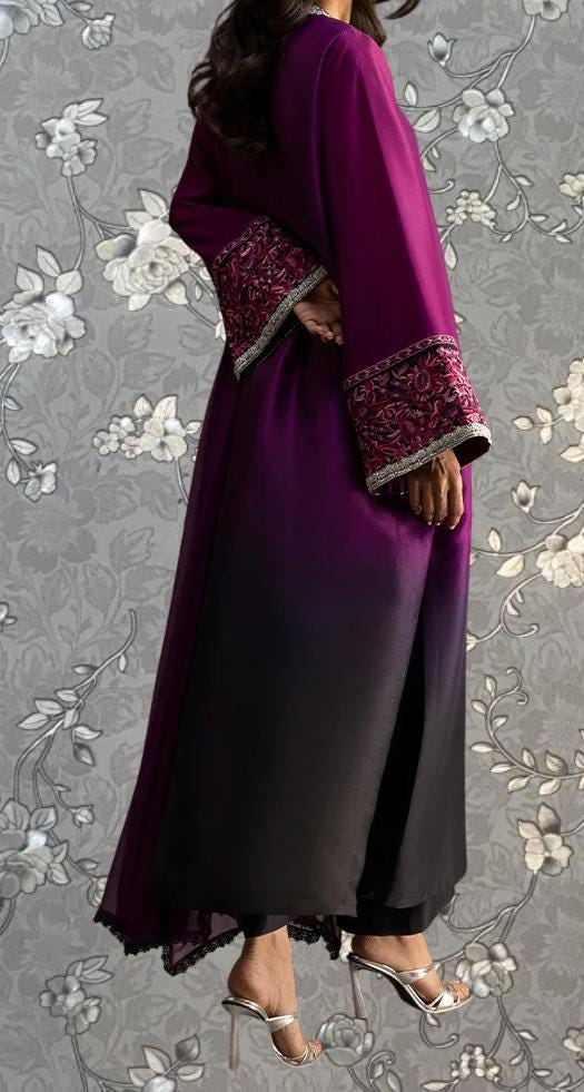 A person wearing a long purple dress with intricate embroidery and a black and purple gradient skirt, standing against a gray floral background.