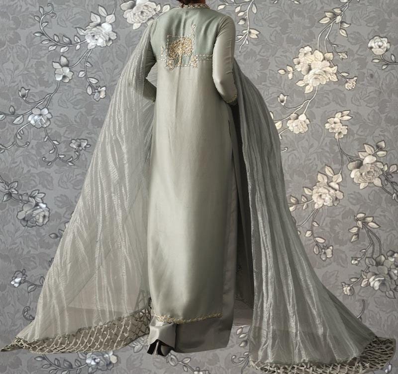 A long, flowing gray dress with a sheer, draped skirt and a matching sheer cape. The dress has a floral pattern on the back and the skirt is made of a shiny, metallic material.