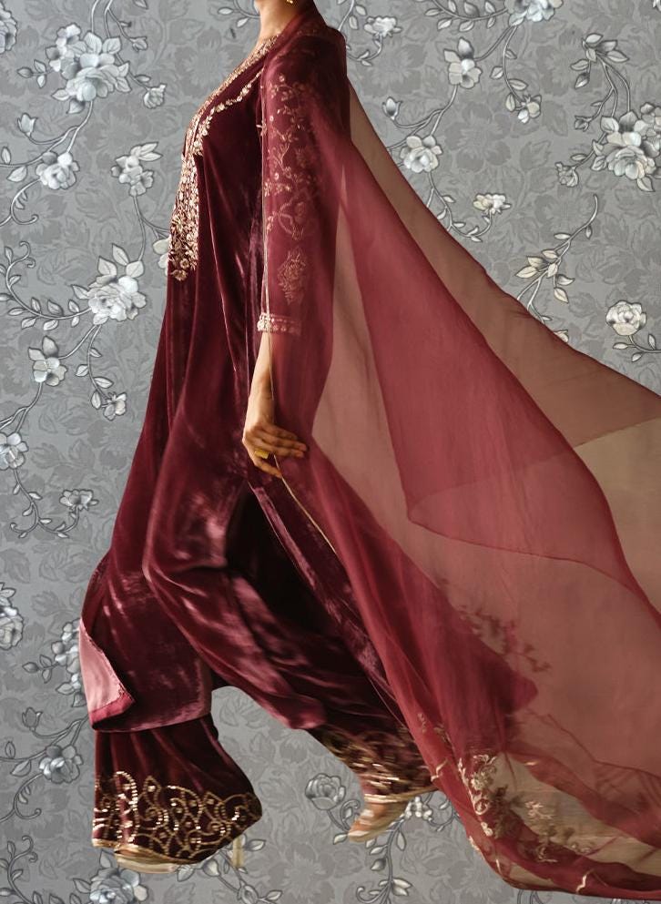 A mannequin wearing a long, burgundy velvet dress with a flowing, sheer cape.