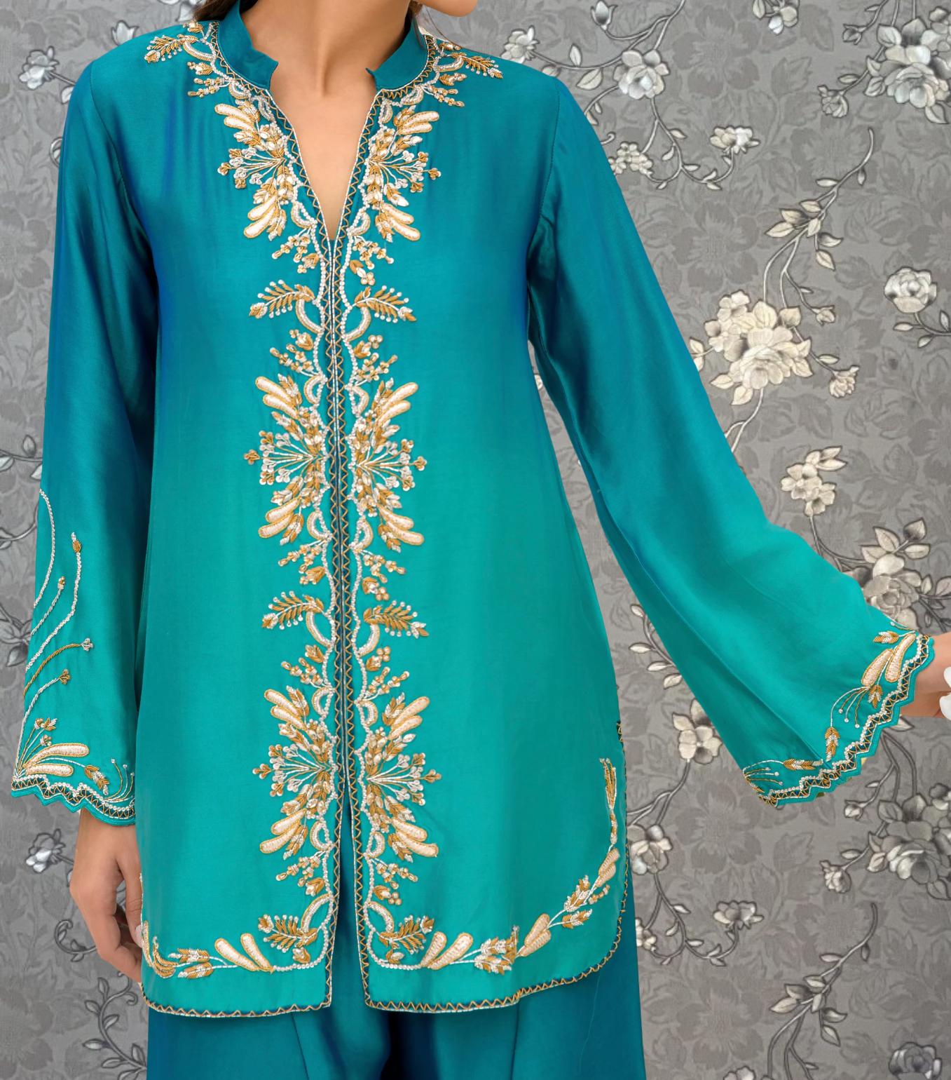 A close-up of a person wearing a teal-colored dress with intricate gold embroidery on the sleeves and collar.