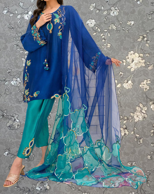 A woman wearing a blue dress with intricate embroidery and a flowing blue and green sheer fabric draped over her.