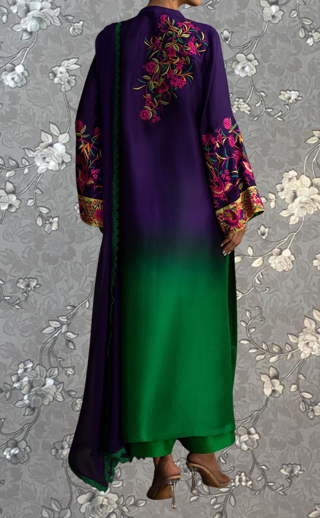 a person wearing a long, colorful dress with floral embroidery on the back. The dress has a gradient of green and purple colors, and the person is standing against a gray floral background.
