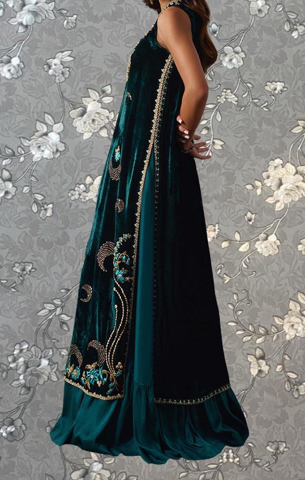 A woman wearing a long, green velvet dress with intricate embroidery and floral patterns.