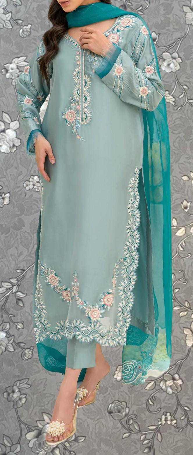A woman wearing a light blue dress with intricate floral embroidery and a matching green shawl.