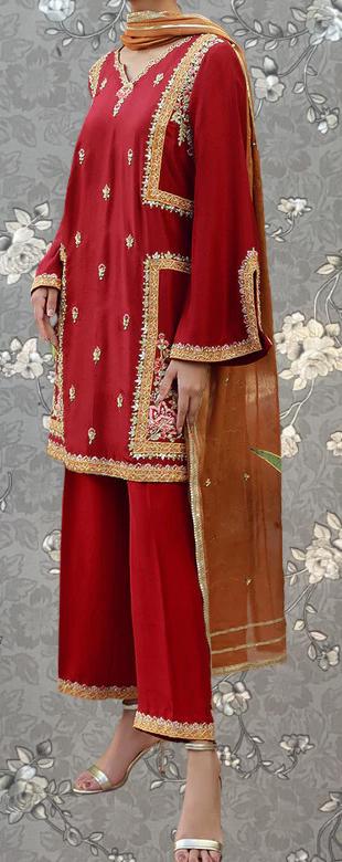 A person wearing a traditional red and gold outfit with intricate embroidery and patterns, standing against a gray floral background.