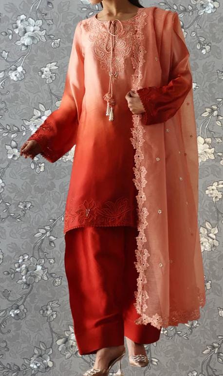 A woman wearing a long, flowing dress with a pink and orange color scheme, featuring intricate embroidery and lace details.