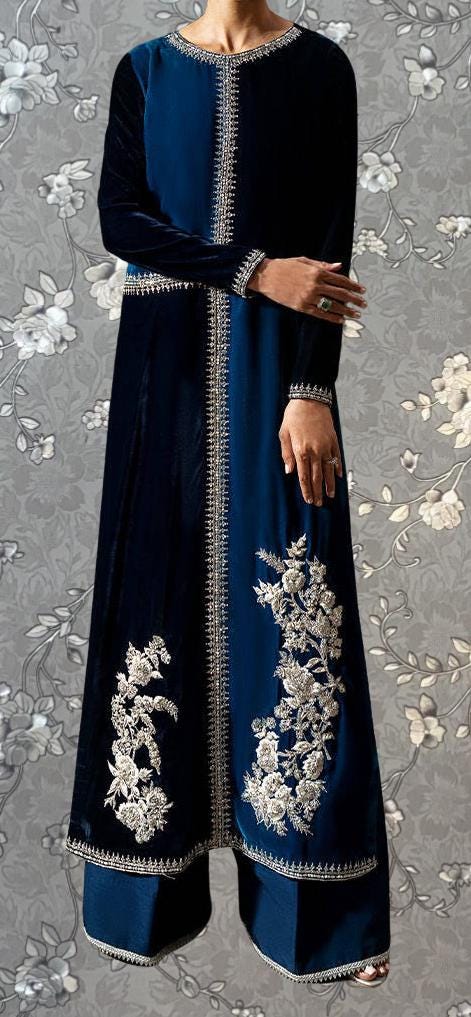 A person wearing a long blue dress with intricate embroidered designs on the sleeves and hem.