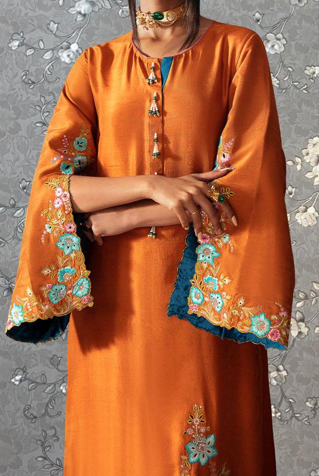 A person wearing an orange dress with intricate embroidered designs on the sleeves and collar.