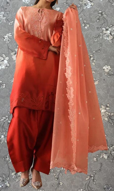 A woman wearing a red and peach-colored dress with a matching shawl, standing against a gray floral background.