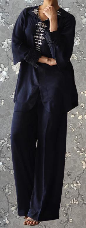 A person wearing a navy blue outfit with a floral pattern on the top and pants, standing against a gray floral background.