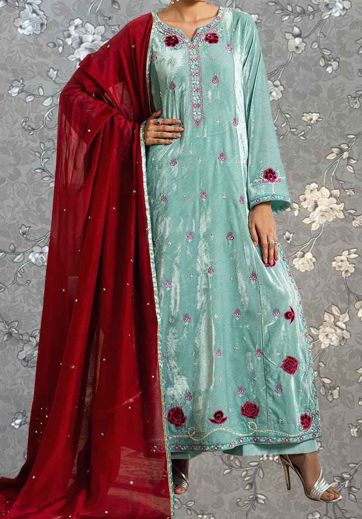 A woman wearing a long, light blue dress with red floral embroidery and a matching red shawl draped over her shoulders.