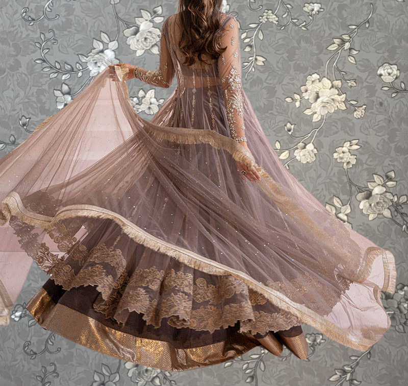 A woman wearing a long, flowing dress with intricate lace and floral embroidery stands against a floral background.