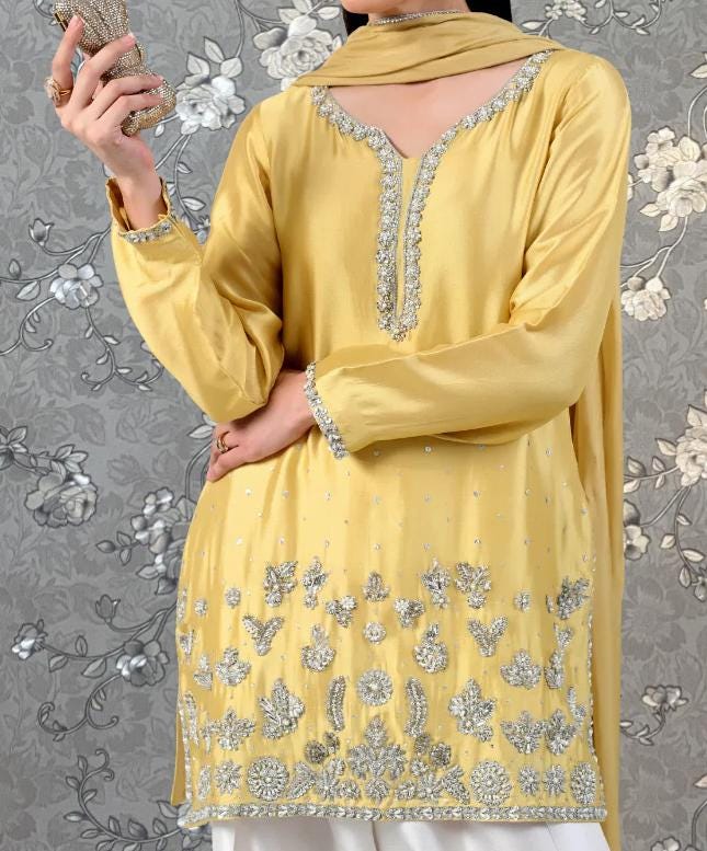 A person wearing a yellow dress with intricate silver embroidery and a matching yellow scarf.