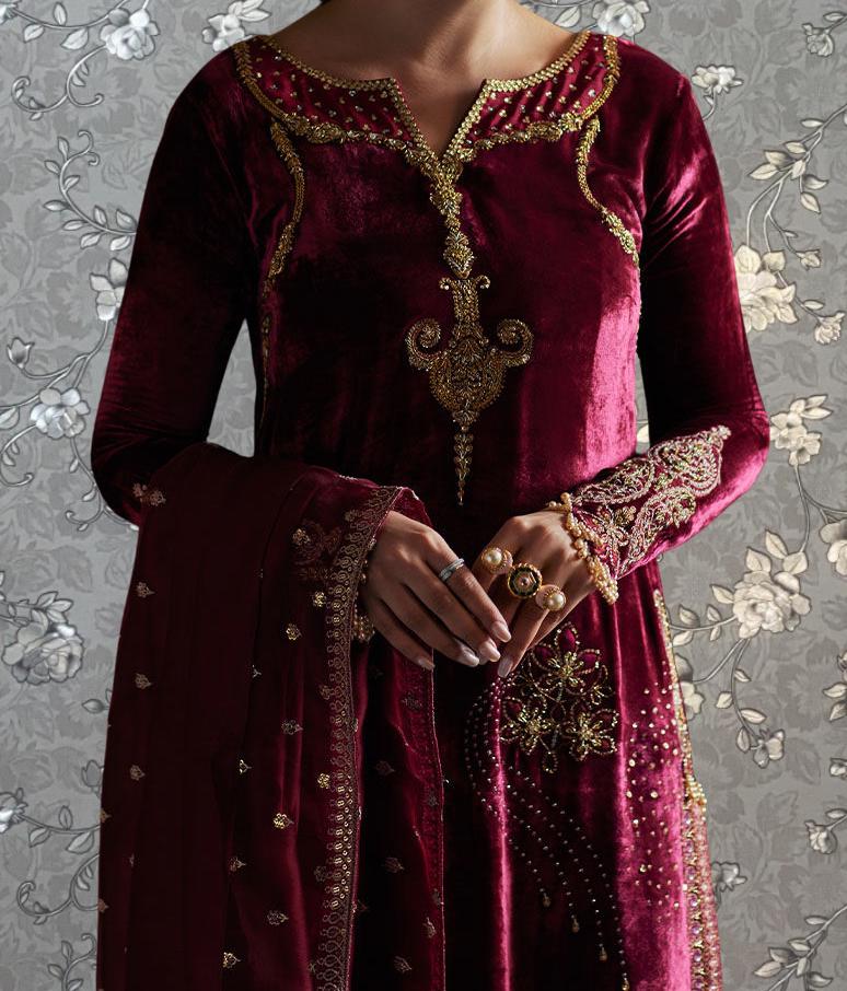 A woman wearing a long, burgundy velvet dress with gold embroidery and jewelry, including a large gold brooch on the front.