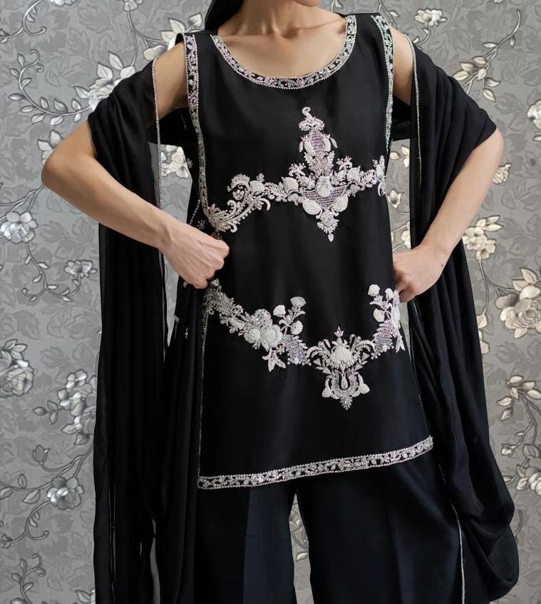 A person wearing a black dress with intricate embroidered designs on the front.