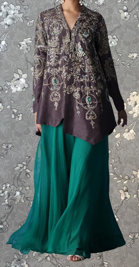 A woman wearing a long, dark purple dress with intricate embroidery and a matching green skirt, standing against a gray floral background.