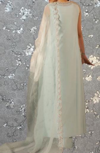 a person wearing a long, light blue dress with a sheer, flowing skirt. The dress has a long train and a delicate, lace-like trim along the back. The background features a gray floral pattern.