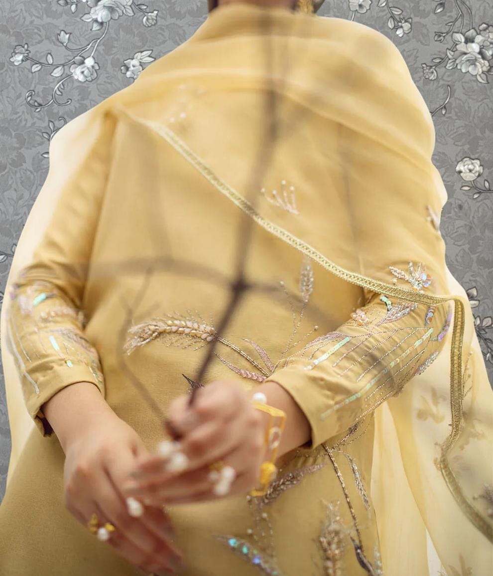 A person wearing a yellow dress with intricate embroidery and a matching yellow shawl is holding a branch in their hands.