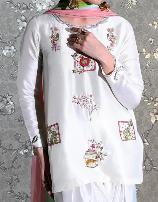 A person wearing a white dress with colorful floral embroidery and a pink scarf around their neck.