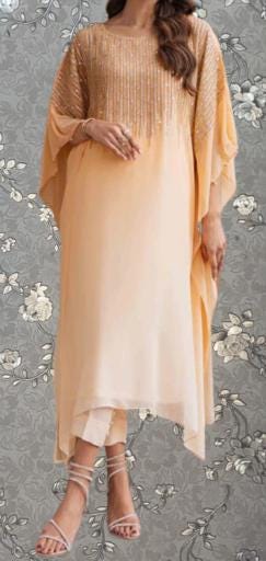 A woman wearing a peach-colored dress with gold embellishments, standing against a gray floral background.