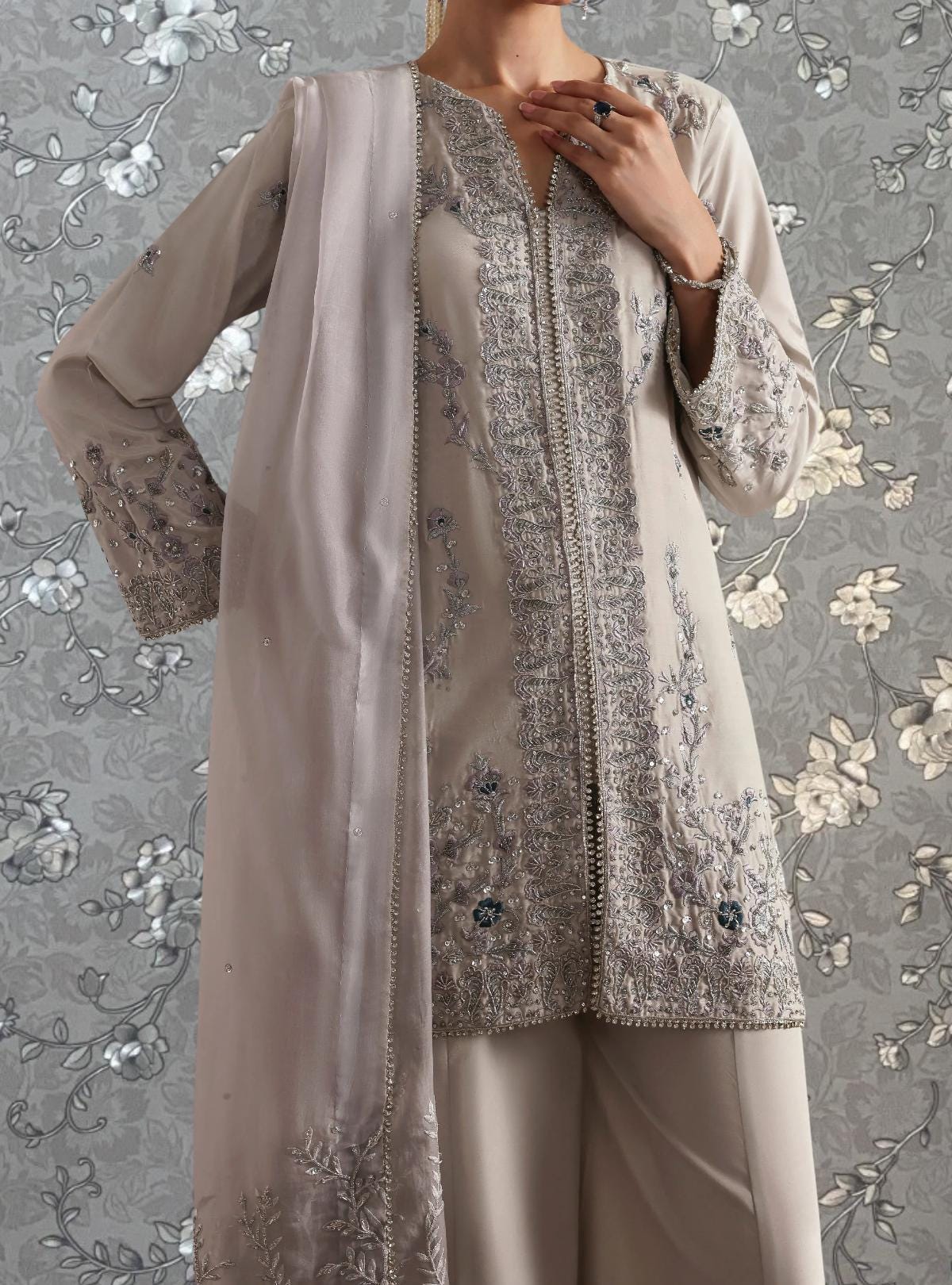 A woman wearing a gray and white patterned dress with intricate embroidery and a matching shawl.