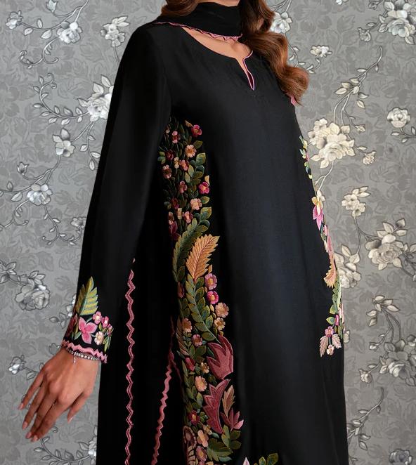 A woman wearing a black dress with intricate floral embroidery on the sleeves and hem.