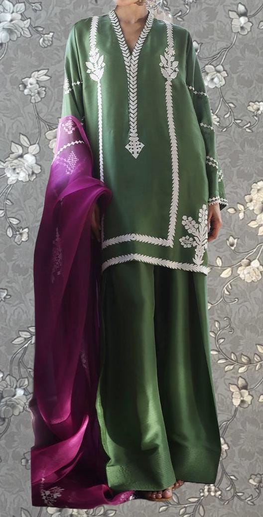 A person wearing a green dress with white embroidered patterns and a matching green shawl draped over their shoulders.