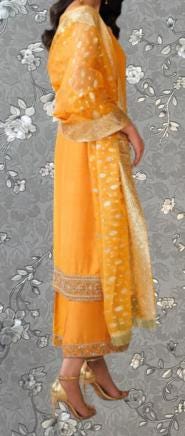 A woman wearing a bright yellow and gold dress with a matching shawl, standing against a gray floral background.