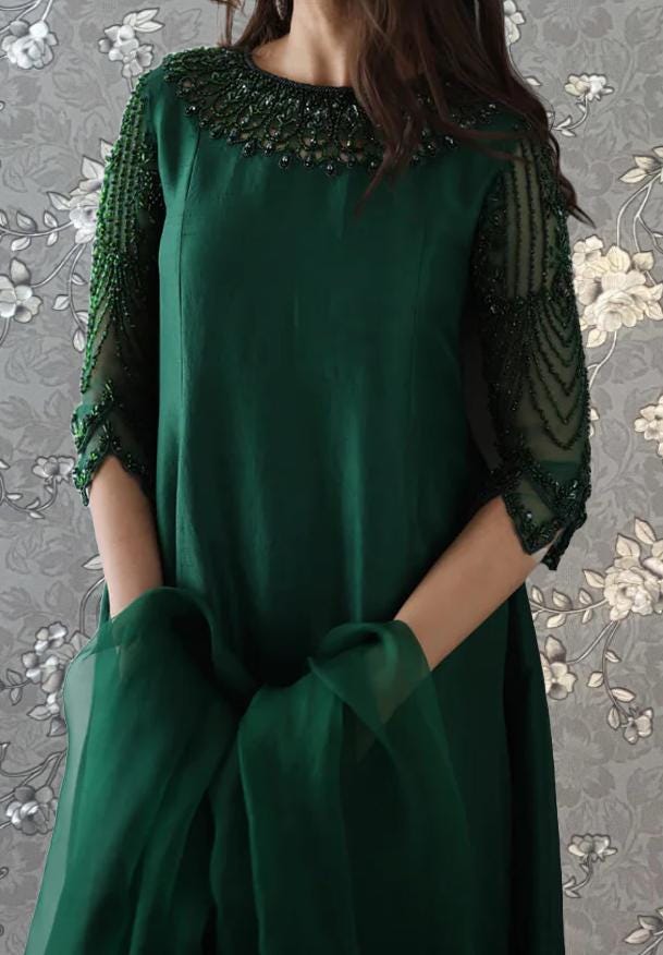 A woman wearing a green dress with intricate beading and embroidery on the neckline and sleeves.