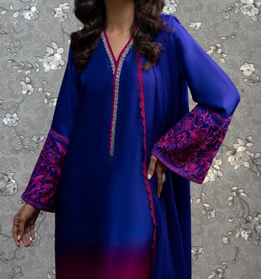 A woman wearing a blue dress with pink floral accents, posing against a gray floral background.