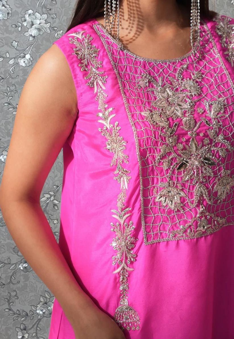 A close-up of a woman wearing a pink dress with intricate embroidery and a floral pattern.