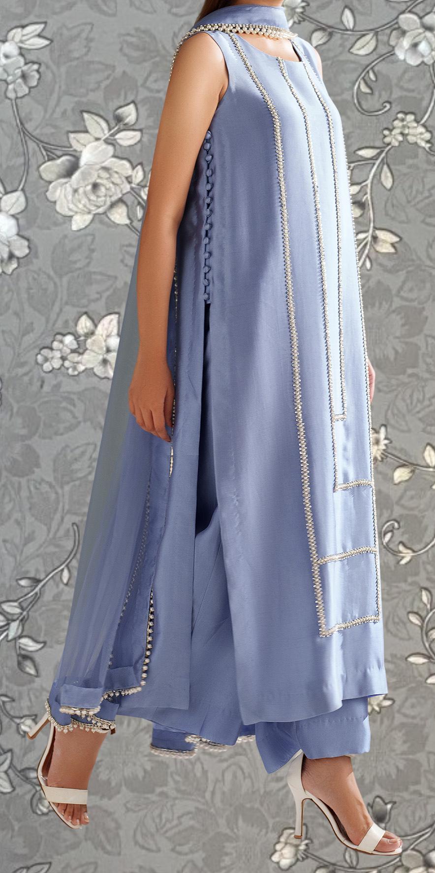 A woman wearing a long, sleeveless blue dress with intricate embroidery and a high neckline, paired with white high heels.