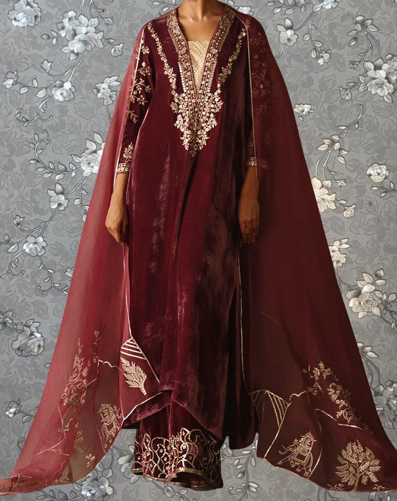 A person wearing a long, burgundy velvet dress with intricate embroidery and a matching cape.