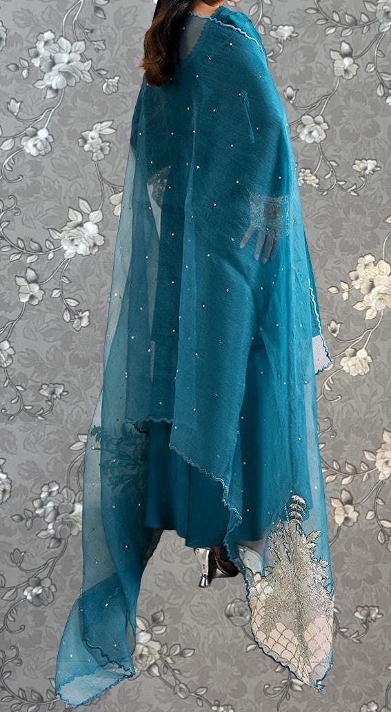 A person wearing a teal-colored dress with a sheer, flowing design and a matching sheer shawl.