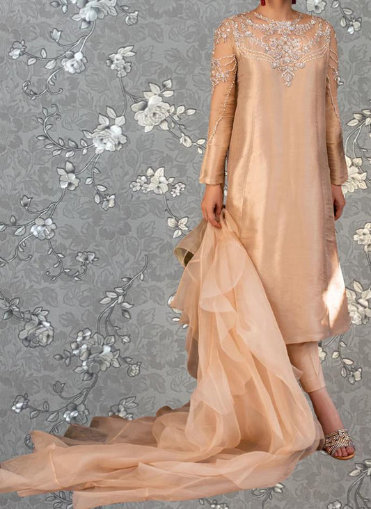 A woman wearing a long, flowing dress with intricate beading and embroidery stands against a gray floral background.