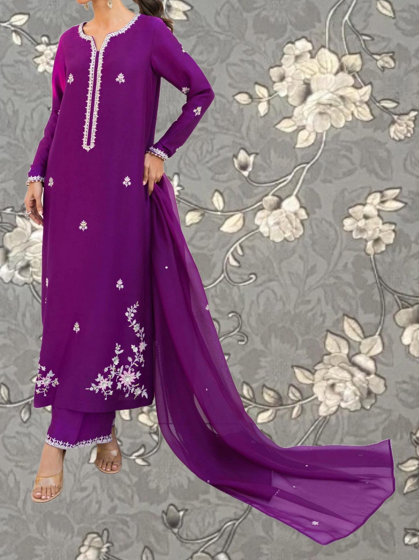 A woman wearing a long purple dress with white floral embroidery stands against a gray floral background.