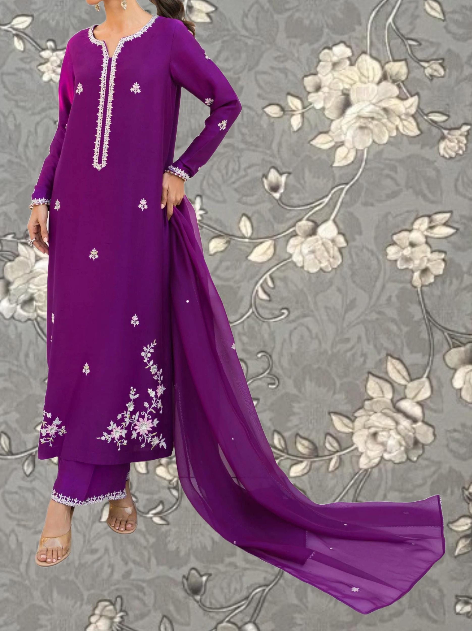A woman wearing a long purple dress with white floral embroidery stands against a gray floral background.