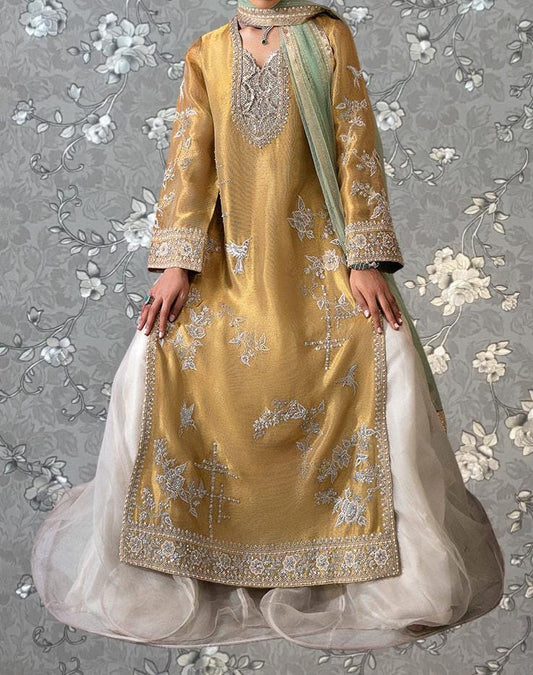 A person wearing a gold and white traditional dress with intricate embroidery stands against a gray floral background.