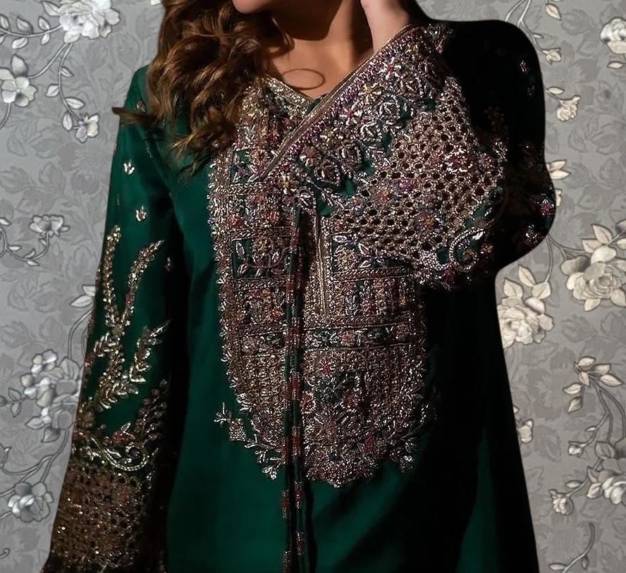 A close-up of a woman wearing a green dress with intricate embroidery and gold accents.